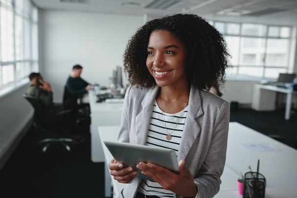 Портрет дружньої успішної молодої чорношкірої бізнес-леді тримає цифровий планшет в руці, дивлячись в офіс
 - Фото, зображення