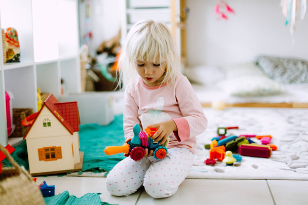 Menina brincando com detalhes de construção coloridos no chão em casa
 - Foto, Imagem