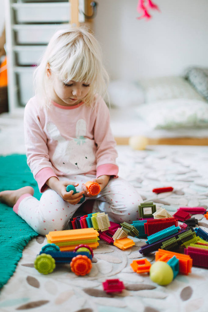 Маленька дівчинка грає з кольоровими деталями будівництва на підлозі вдома
 - Фото, зображення