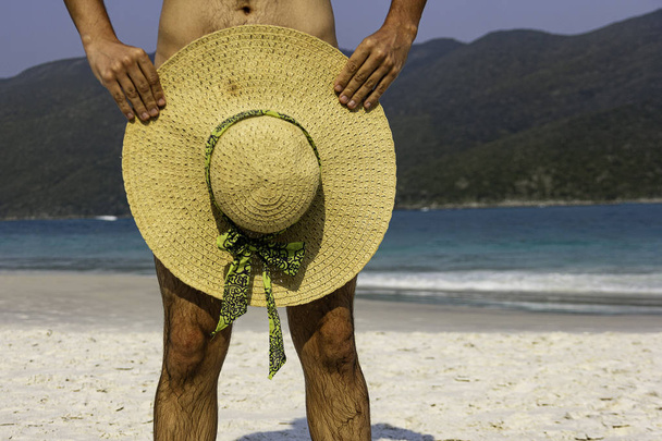 Man in naakt strand met zonnehoed over instimate onderdelen. Nudisten concept. - Foto, afbeelding