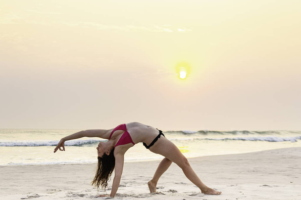 Жінка практикує йогу на пляжі під час заходу сонця
. - Фото, зображення