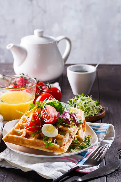 Belgische Waffeln mit Avocado, Eiern, Mikrogrün und Tomaten mit Orangensaft und Tee auf einem Holztisch. perfektes Frühstück für gesunde Ernährung oder Abnehmen. Avocado-Sandwich. - Foto, Bild