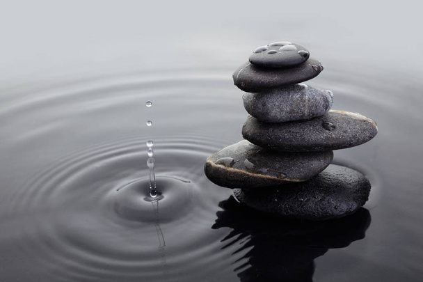 Kamienie Zen w zrównoważonym stosie w wodzie na falowanej powierzchni wody i spadku wody. - Zdjęcie, obraz
