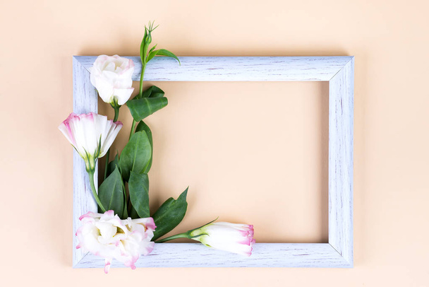 Empty white frame and flowers eustoma on beige paper background with copy space. Holiday concept - Φωτογραφία, εικόνα