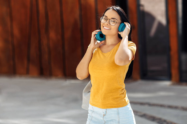 Charming brunette young woman with bright smile dressed in casual clothes listening to music with headphones and smiling. - 写真・画像