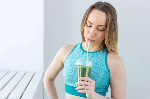 Gezond, fitness en detox concept-close-up van de jonge vrouw in sportkleding met groene smoothie binnenshuis - Foto, afbeelding
