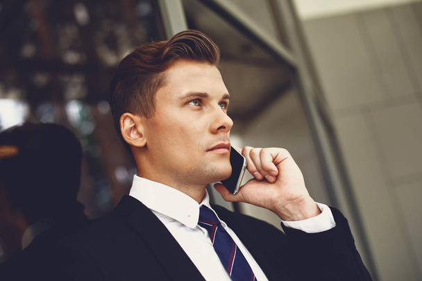 Close up of serious young man in black suit talking on the phone - Fotoğraf, Görsel