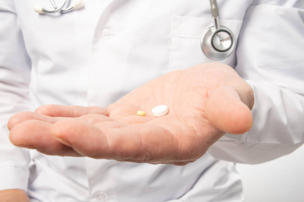 The doctor in white clothes, and blue gloves, with a stethoscope on his neck, holds out pills. Close up - Foto, afbeelding