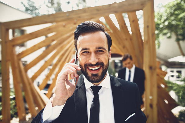 Close up of bearded young man smiling and having pleasant phone talk - Photo, image
