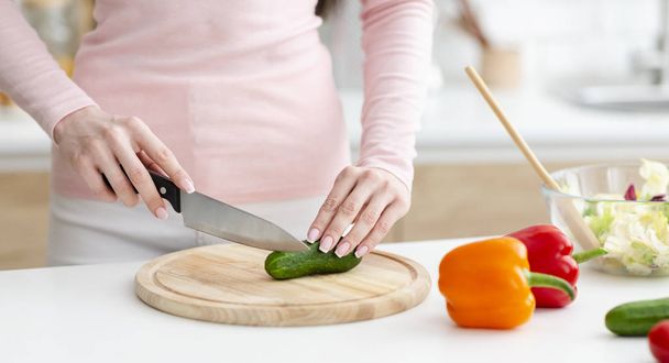 Vrouw snijden verse groenten voor salade op houten plank - Foto, afbeelding