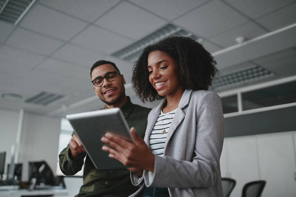 Portrait of smiling professional young African American businesswoman showing data on digital tablet to male colleague in office - Фото, изображение