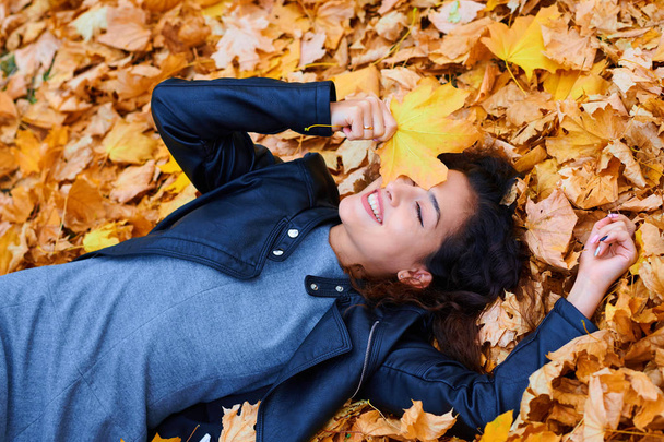 Frau liegt mit Herbstlaub im Stadtpark, Außenporträt - Foto, Bild