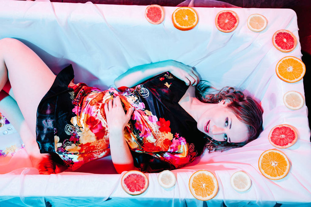 Mujer joven relajándose en la bañera de hidromasaje con rodajas de naranjas. Concepto de solidez
. - Foto, imagen