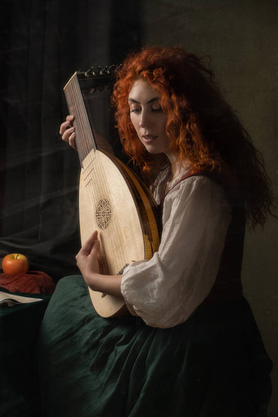 Red-haired girl in a historical suit plays the lute. Renaissance painting style - Foto, imagen