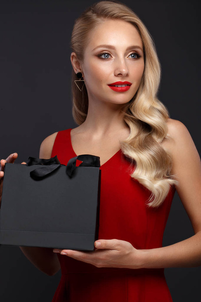 Beautiful girl with blond hair, classic make-up in a elegant red dress and shopping bag. Beauty face. - Foto, afbeelding