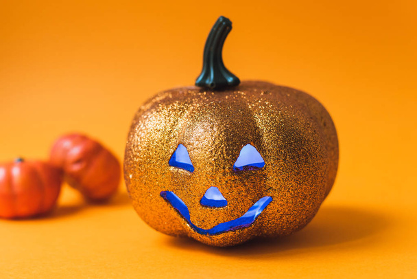 Enge glimmende Halloween pompoen speelgoed. Jack-o '-lantaarn op een oranje achtergrond met blauwe lichtgevende ogen met plaats voor tekst - Foto, afbeelding
