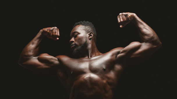 Siyah stüdyo arka plan üzerinde kasları esneyen atletik afrika fitness modeli - Fotoğraf, Görsel