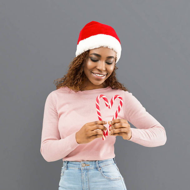 Fille souriante dans le chapeau de Père Noël faire coeur avec des bonbons de Noël
 - Photo, image