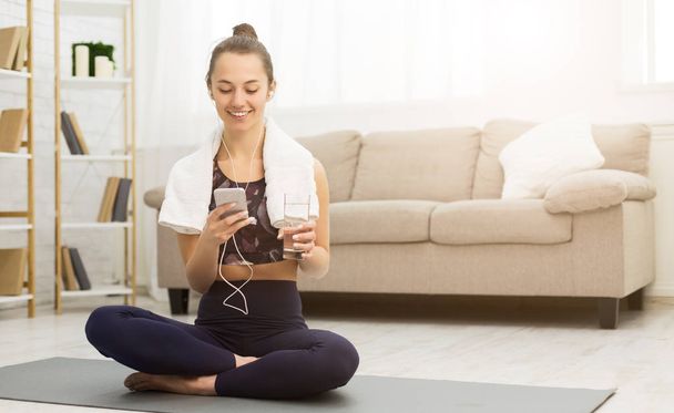 Woman resting after home workout with water and phone - Φωτογραφία, εικόνα