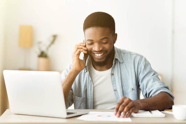 Веселий афроамериканець бізнесмен розмовляє по телефону і читанні документації - Фото, зображення