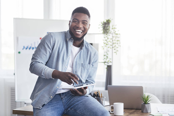 Веселый черный работник, использующий цифровой планшет в офисе и смеющийся
 - Фото, изображение