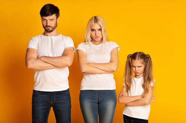 Θυμωμένος οικογένεια στέκεται διασχίζοντας τα χέρια συνοφρυωμένο σε κίτρινο στούντιο φόντο - Φωτογραφία, εικόνα