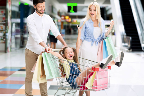 Батьки їзда збуджена дочка в кошик ходьба в торговому центрі
 - Фото, зображення