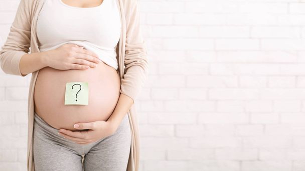 Schwangere umarmt ihren Bauch mit Fragezeichen - Foto, Bild