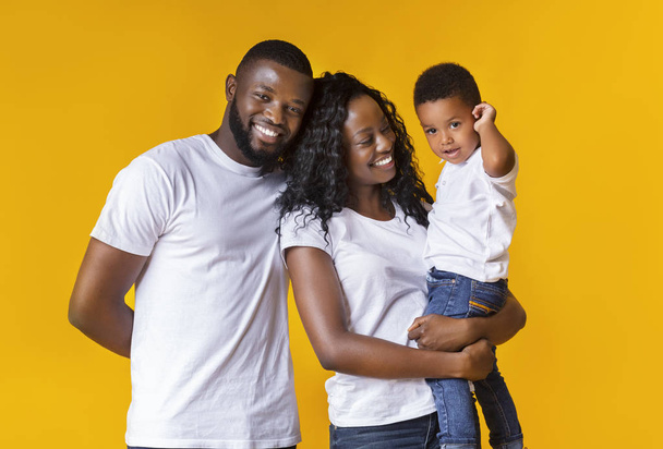 Joyeux jeunes parents avec mignon petit fils sur fond jaune
 - Photo, image