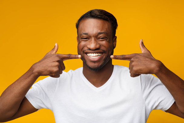 Homem negro apontando os dedos em seu sorriso branco dos dentes, estúdio
 - Foto, Imagem