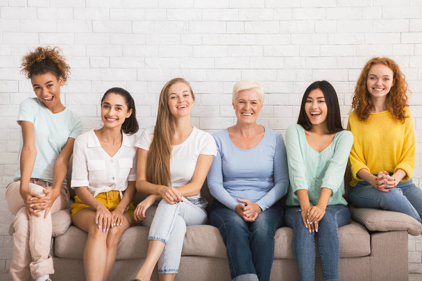 Mujeres sonrientes y diversas sentadas en un sofá sobre una pared de ladrillo blanco
 - Foto, imagen