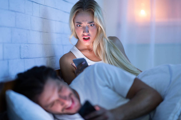 Kateellinen tyttöystävä kiinni poikaystävä tekstailu naisten kanssa makaa sängyssä
 - Valokuva, kuva