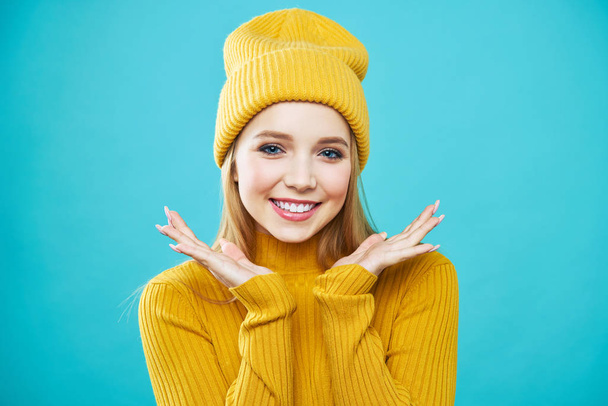 Portrét nádherné dívky ve žlutém klobouku a svetru, když se dívala na kameru a usmívala se roztomile. - Fotografie, Obrázek
