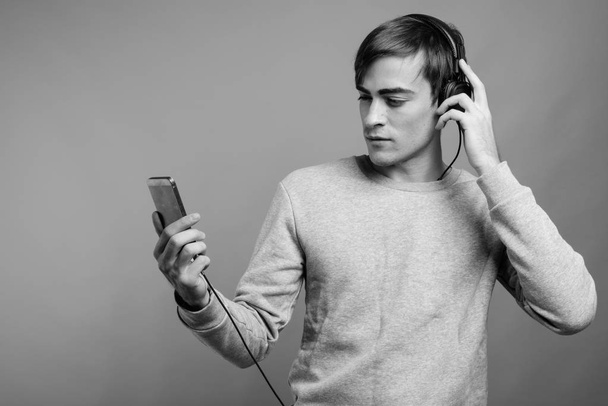 Young handsome man listening to music and ready for gym against gray background - Foto, afbeelding