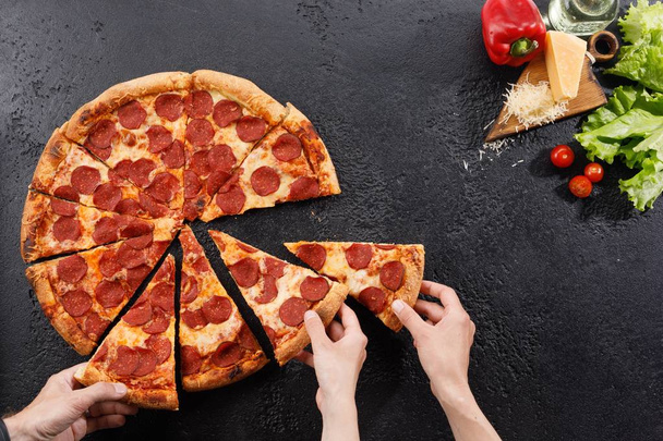 Pepperoni pizza on a black background texture. Still life with hands and ingredients. Copy space. - Foto, imagen