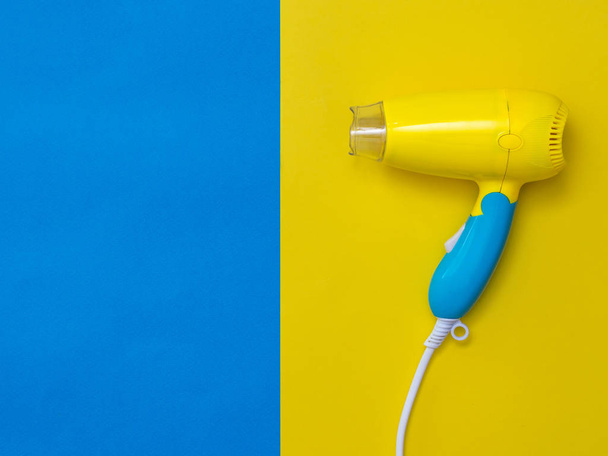 Secador de pelo amarillo-azul sobre un fondo amarillo junto al azul
. - Foto, Imagen