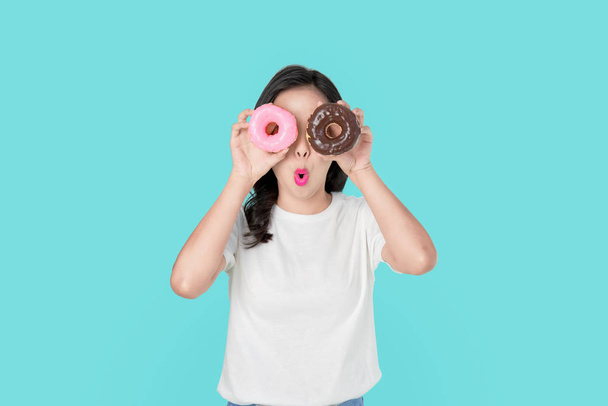 Vrolijke mooie Aziatische vrouw die haar ogen bedekt met kleurrijke donuts op blauwe achtergrond. - Foto, afbeelding