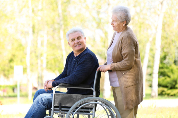 Mature man in wheelchair and senior woman at park on sunny day - Photo, Image