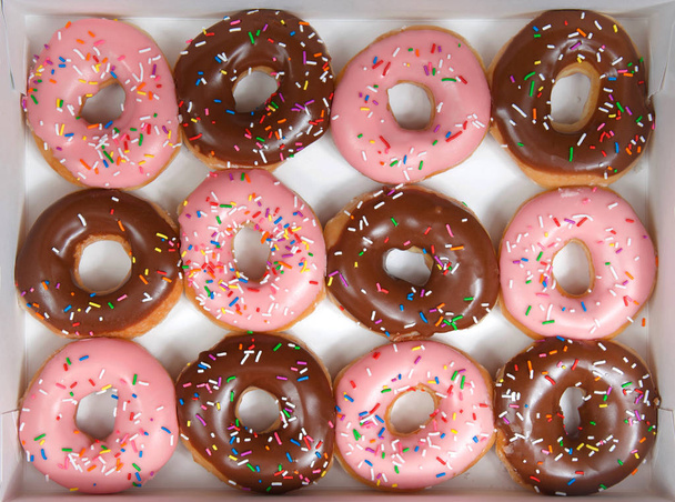 Flach lag ein Dutzend glasierte Donuts, abwechselnd Erdbeere und Schokolade in einer weißen Schachtel isoliert. sind Donuts, die zu einer neuen Modeerscheinung oder zum neuen Trend werden. Gourmet-Stil ausgefallene Donuts. - Foto, Bild