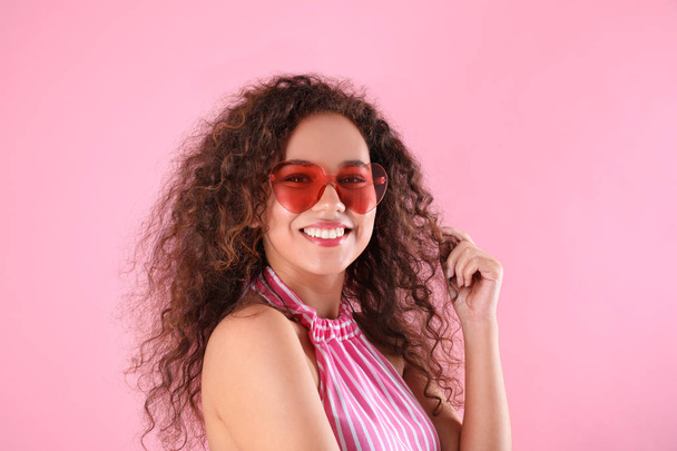 Young beautiful African-American woman wearing heart shaped glasses on pink background - Foto, afbeelding