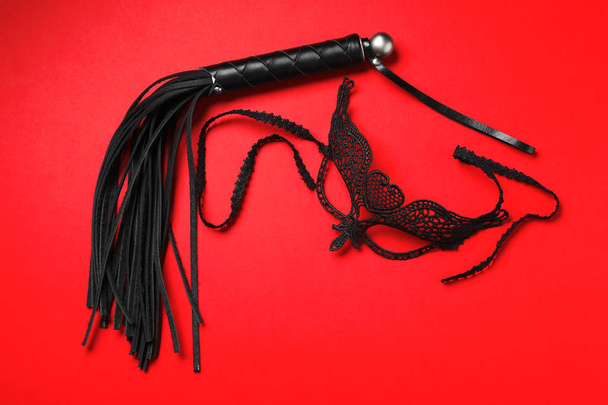 Black whip and lace mask on ed background, flat lay. Accessories for sexual role play - Foto, Bild