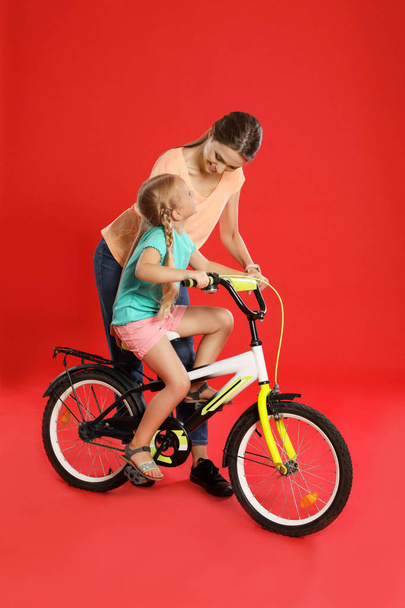 Young mother teaching daughter to ride bicycle on red background - Photo, Image