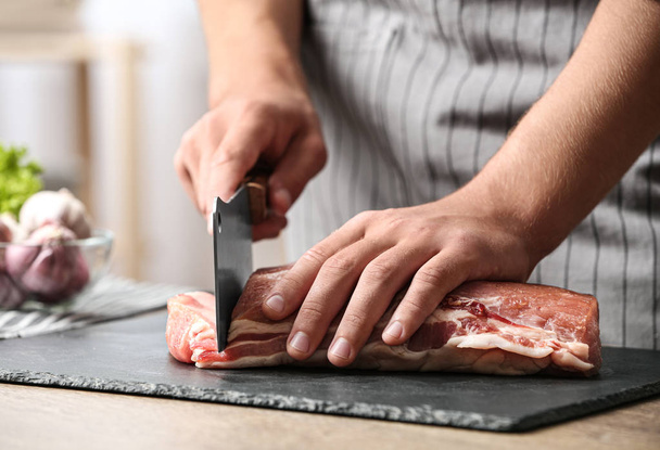 Man cutting fresh raw meat on table in kitchen, closeup - Foto, afbeelding