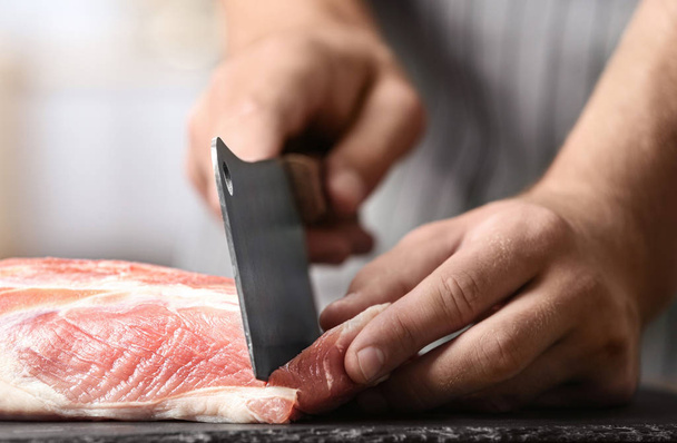 Man cutting fresh raw meat on table in kitchen, closeup - Foto, afbeelding