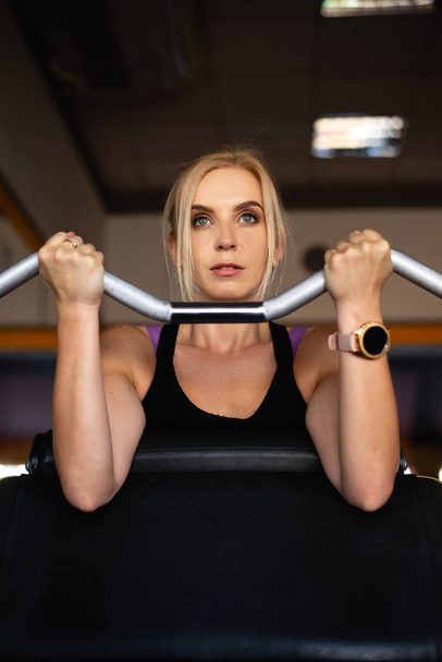 Spor salonunda genç bir kız meşgul, güçlü eller ağırlık kaldırıyor, odaklanmış bir bakış. - Fotoğraf, Görsel