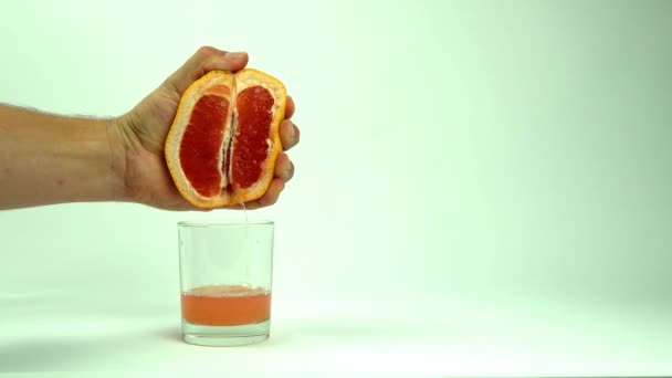 man knijpende de helft van sappige grapefruit om glas te legen op witte achtergrond, close-up - Video