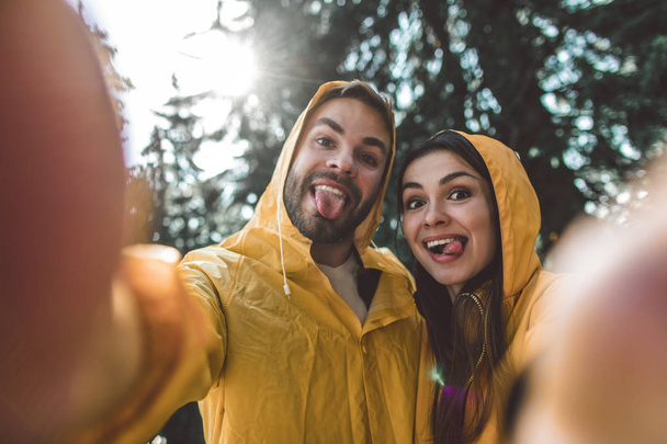 Traveler couple making funny selfie in raincoats - Foto, imagen