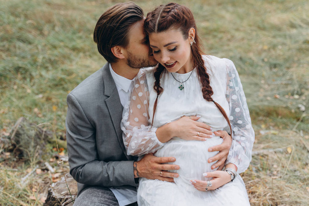 beautiful pregnant woman in white dress with handsome man sitting on a stump - Foto, Bild