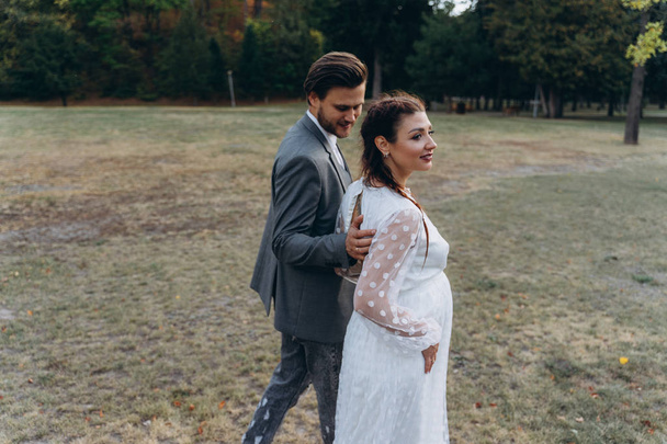 beautiful pregnant woman in white dress with handsome man walking in park - Фото, зображення