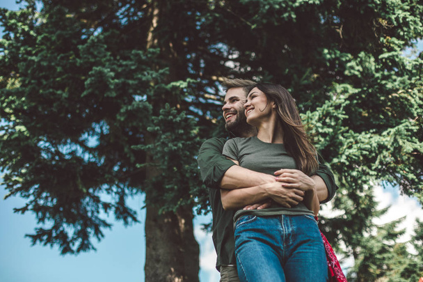Casal amante de pé em abraço perto de árvore verde
 - Foto, Imagem